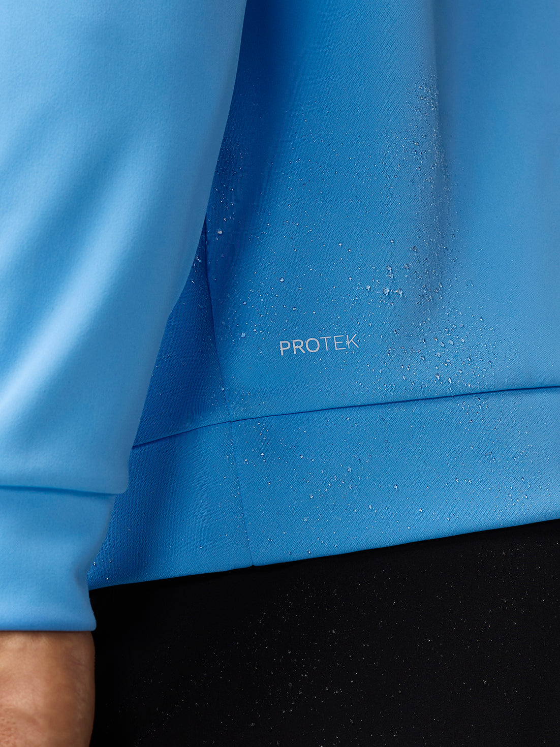 Close-up of blue fabric with water droplets and PROTEK label highlighting water resistance