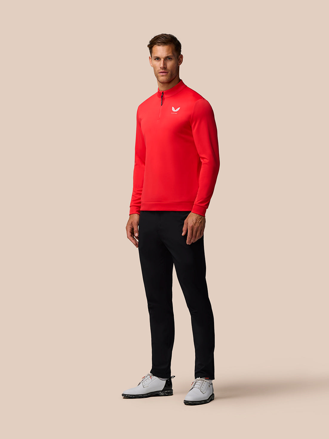 Male model wearing bright red golf long sleeve quarter zip top with stand collar and Castore logo on left chest