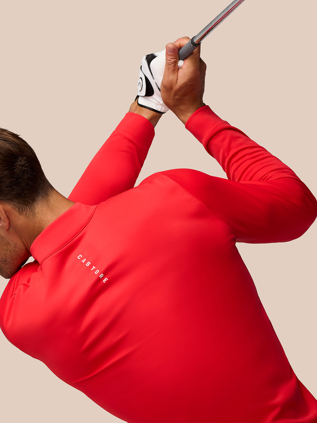 Golfer wearing a red Castore Golf Club Classic 1/4 Zip Top mid swing gripping a golf club