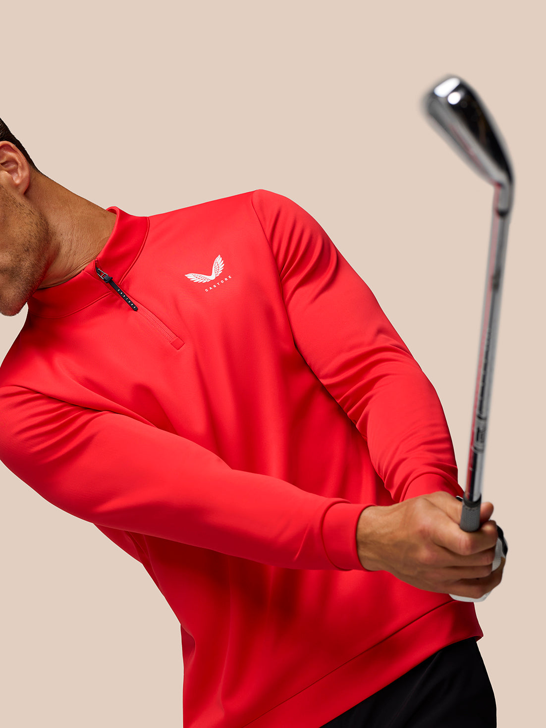 Close up of red Castore Golf Club Classic 1/4 Zip Top with left chest logo as golfer holds a golf club