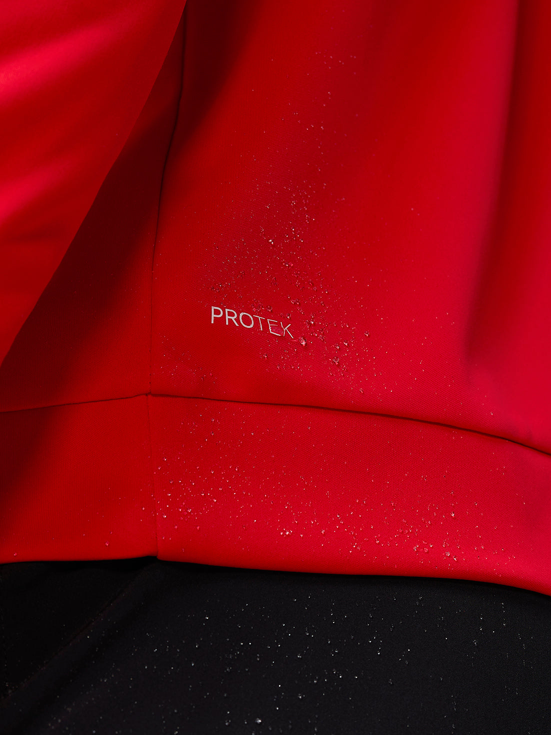 Close up of red Protek fabric with water droplets on the Castore Golf Club Classic top