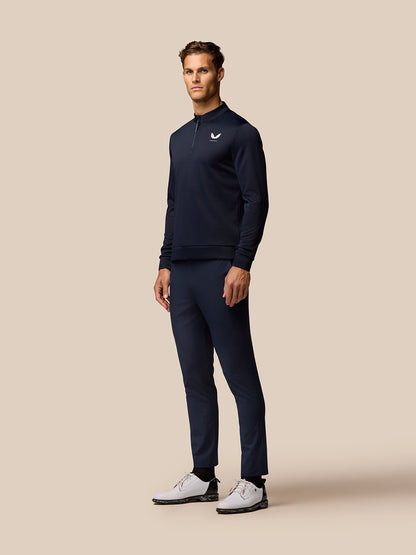 Full length shot of a man in navy golf top and pants with a small Castore logo on the chest and white golf shoes