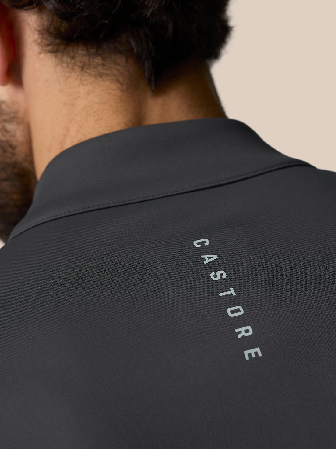 Close-up of a dark golf top showing stand collar and Castore branded zip pull on the back shoulder area.
