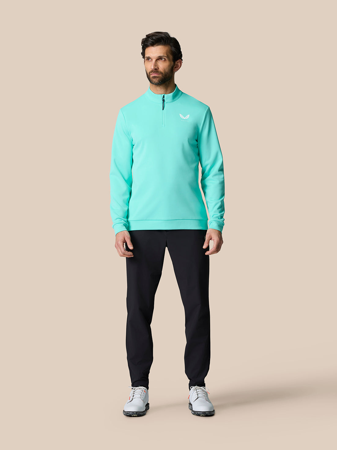 Male model wearing light aqua Golf Club Classic quarter zip top with black pants in a studio setting.