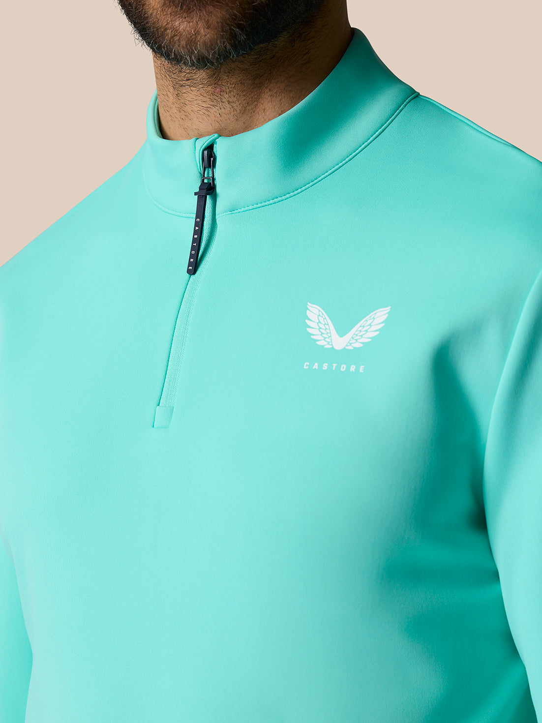 Light aqua Golf Club Classic quarter zip top close-up showing stand collar zipper and Castore logo on chest.
