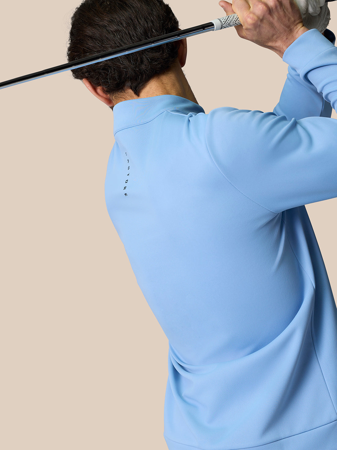 Back view of a golfer in sky blue golf top holding a club behind the head with Castore branding along the back.