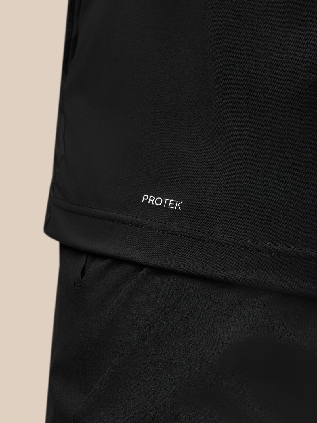 Close-up of the black Pinnacle Gilet fabric with Protek branding near the hem and the front zipper