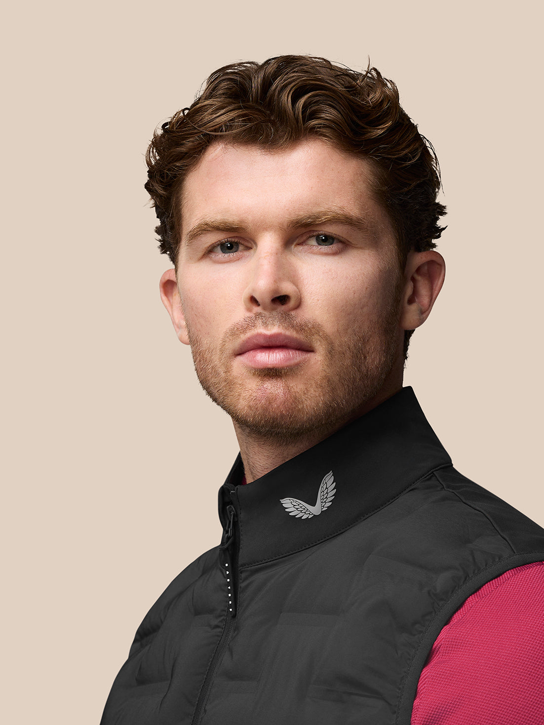 Side view of a man in a black Pinnacle Gilet with pink sleeves visible; CASTORE branding runs vertically along the upper back.