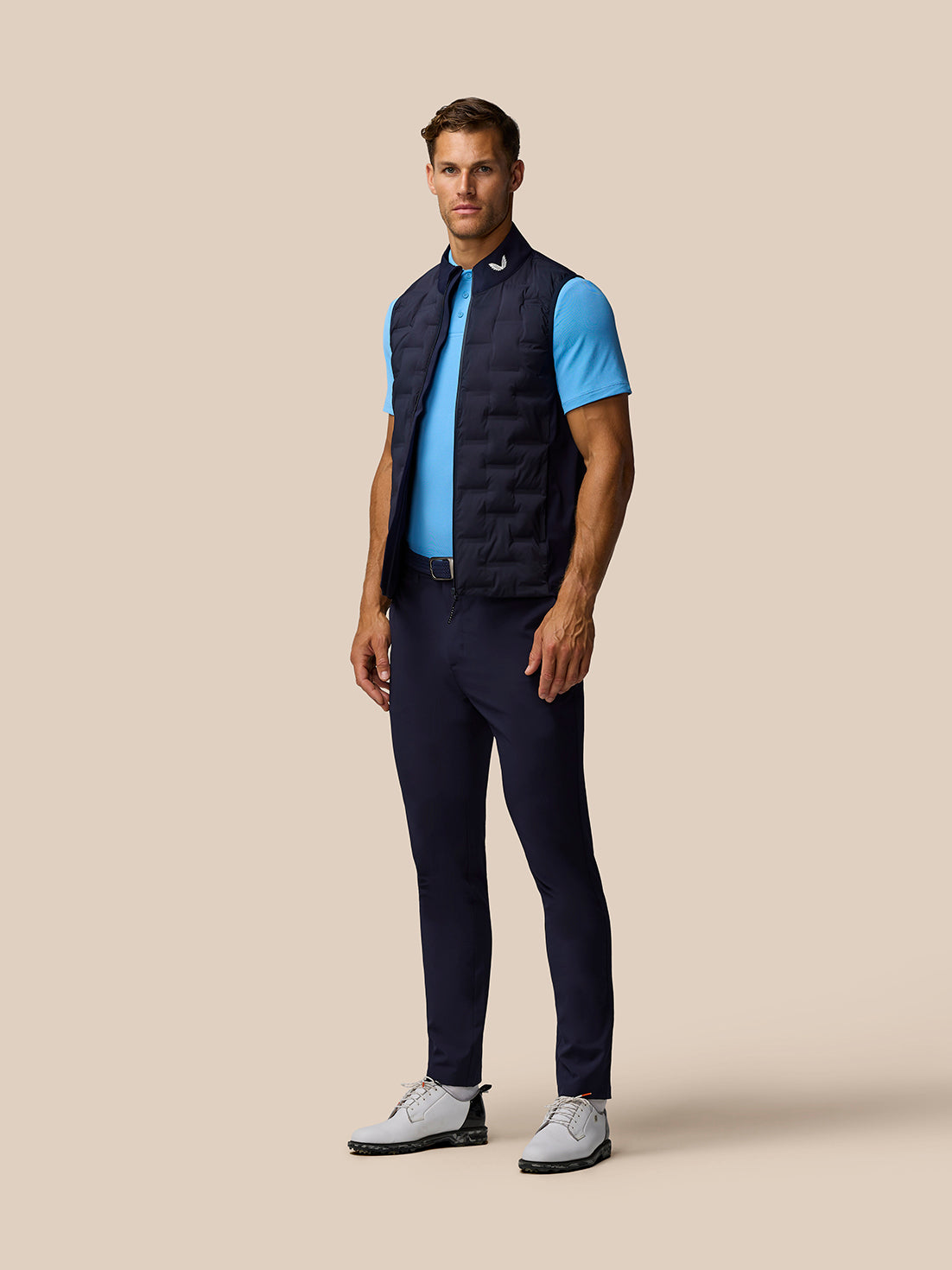 Full body side view of male model in navy Pinnacle Gilet over blue polo on beige background