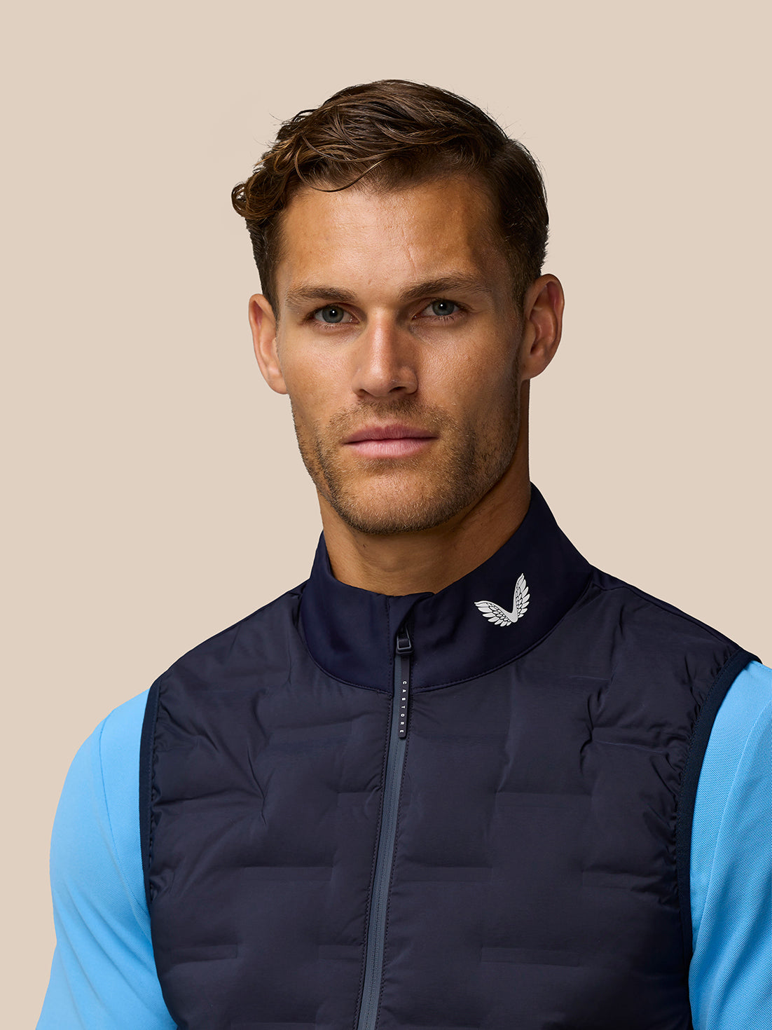 Close-up of a man wearing a navy quilted sleeveless golf gilet with a stand collar and Castore branding at the collar.
