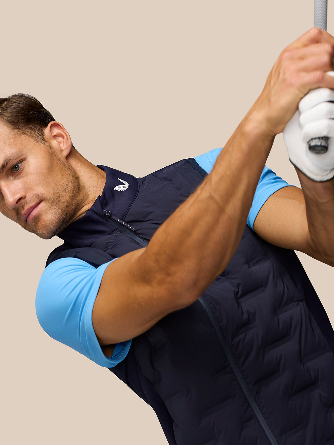 Man wearing midnight navy Pinnacle Golf Gilet over a light blue shirt, front zip visible and collar logo.