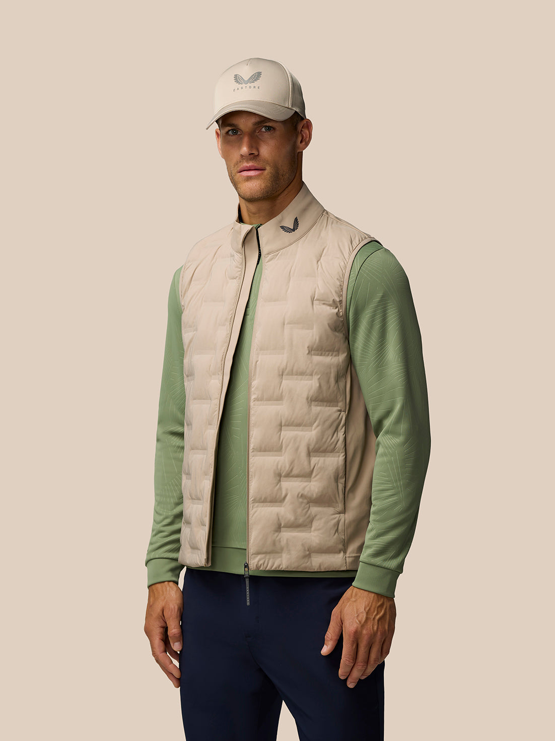 Male model wearing Mushroom Golf Pinnacle Gilet over a green long sleeve, showing the quilted front and funnel collar.