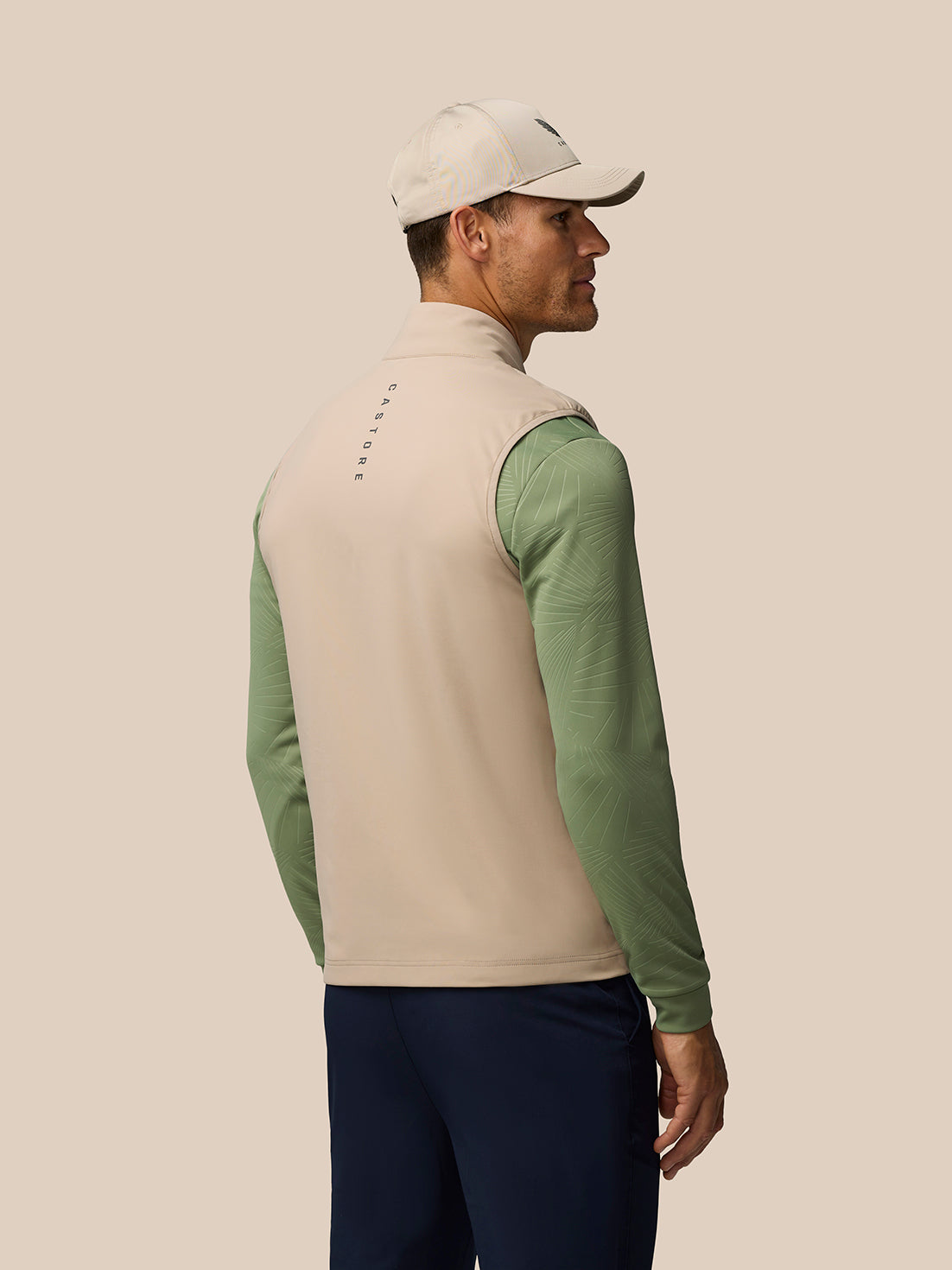 Back view of a model wearing Mushroom Pinnacle Lightweight Hybrid Gilet with beige body and green sleeves.