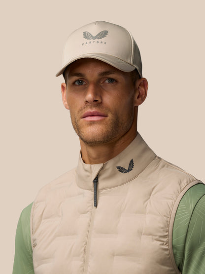 Close-up of male model wearing Mushroom Golf Pinnacle Gilet and cap, highlighting collar logo.