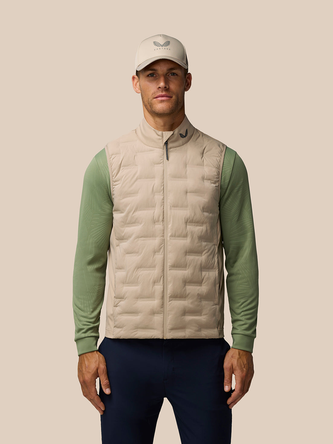 Male model in Mushroom Golf Pinnacle Gilet with full-zip front and quilted panels, cap visible.