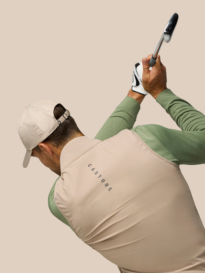 Golfer wearing mushroom Pinnacle Gilet and beige cap mid backswing.