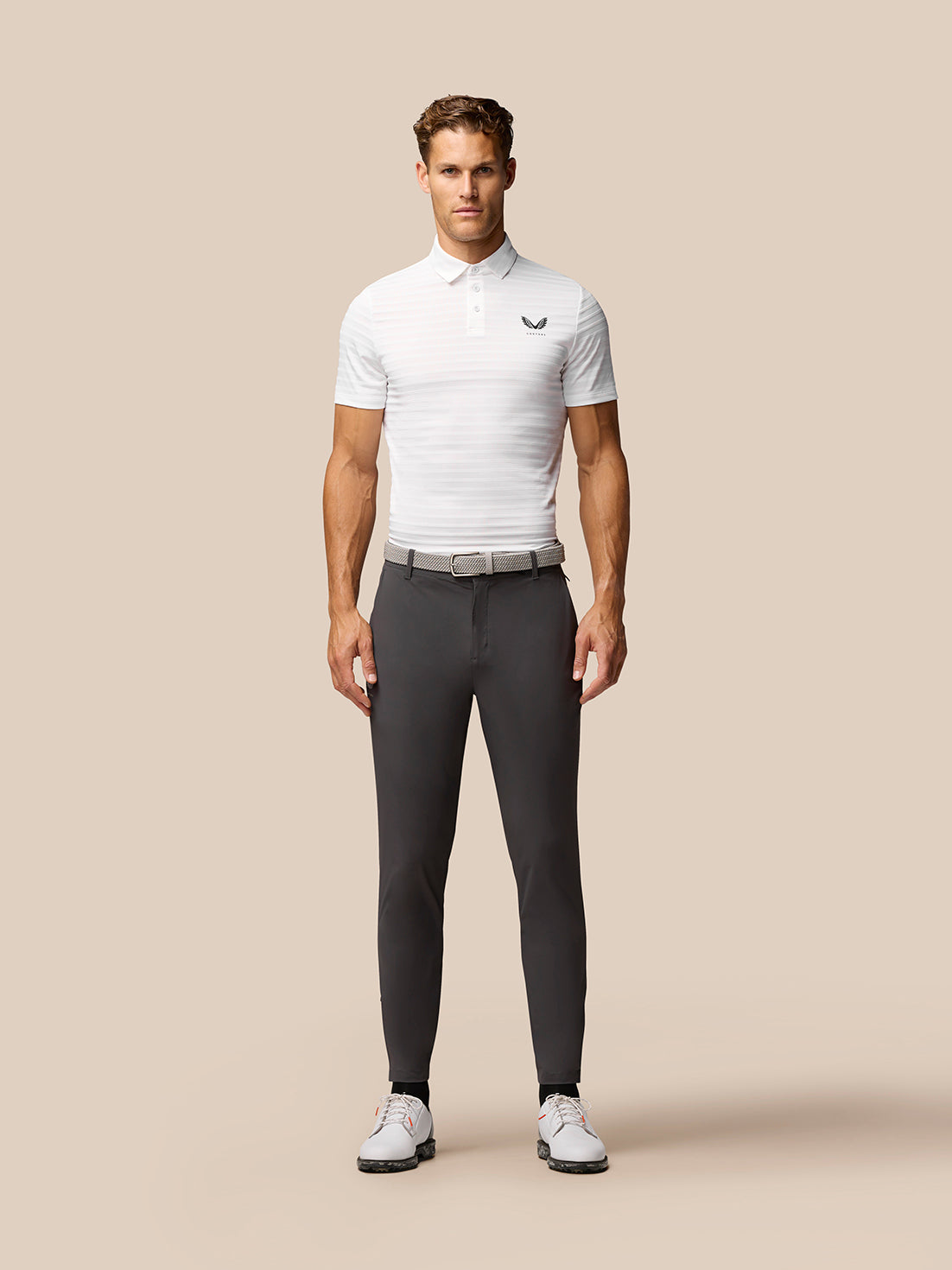 Model wearing charcoal golf joggers with a white polo shirt and belt, front view