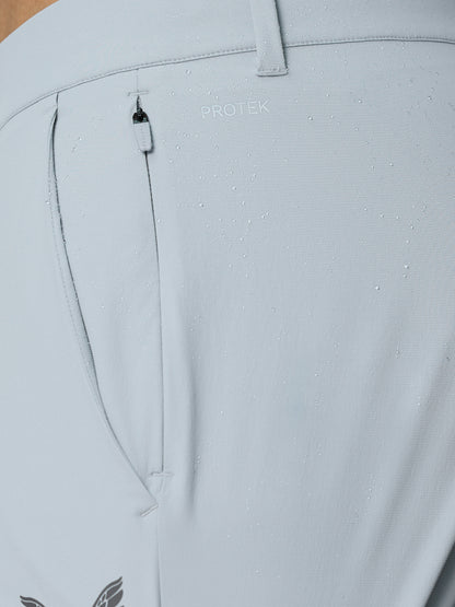 Close up of light grey golf trousers fabric with water droplets, PROTEK branding, belt loop and small zip pocket.