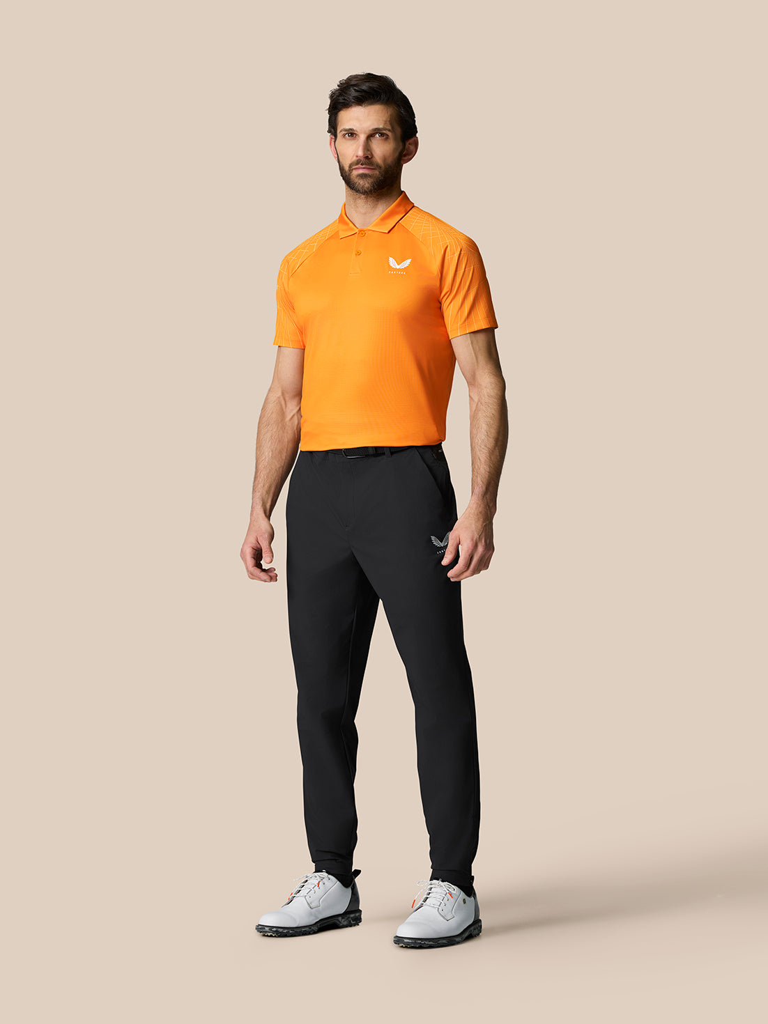 Full-body view of a male model wearing an orange polo and black Golf Pinnacle Trousers.