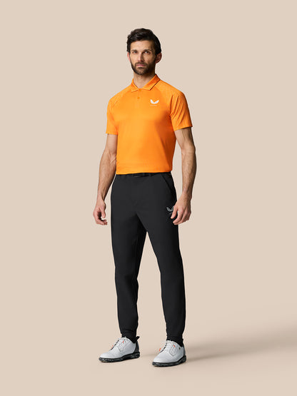 Full-body view of a male model wearing an orange polo and black Golf Pinnacle Trousers.