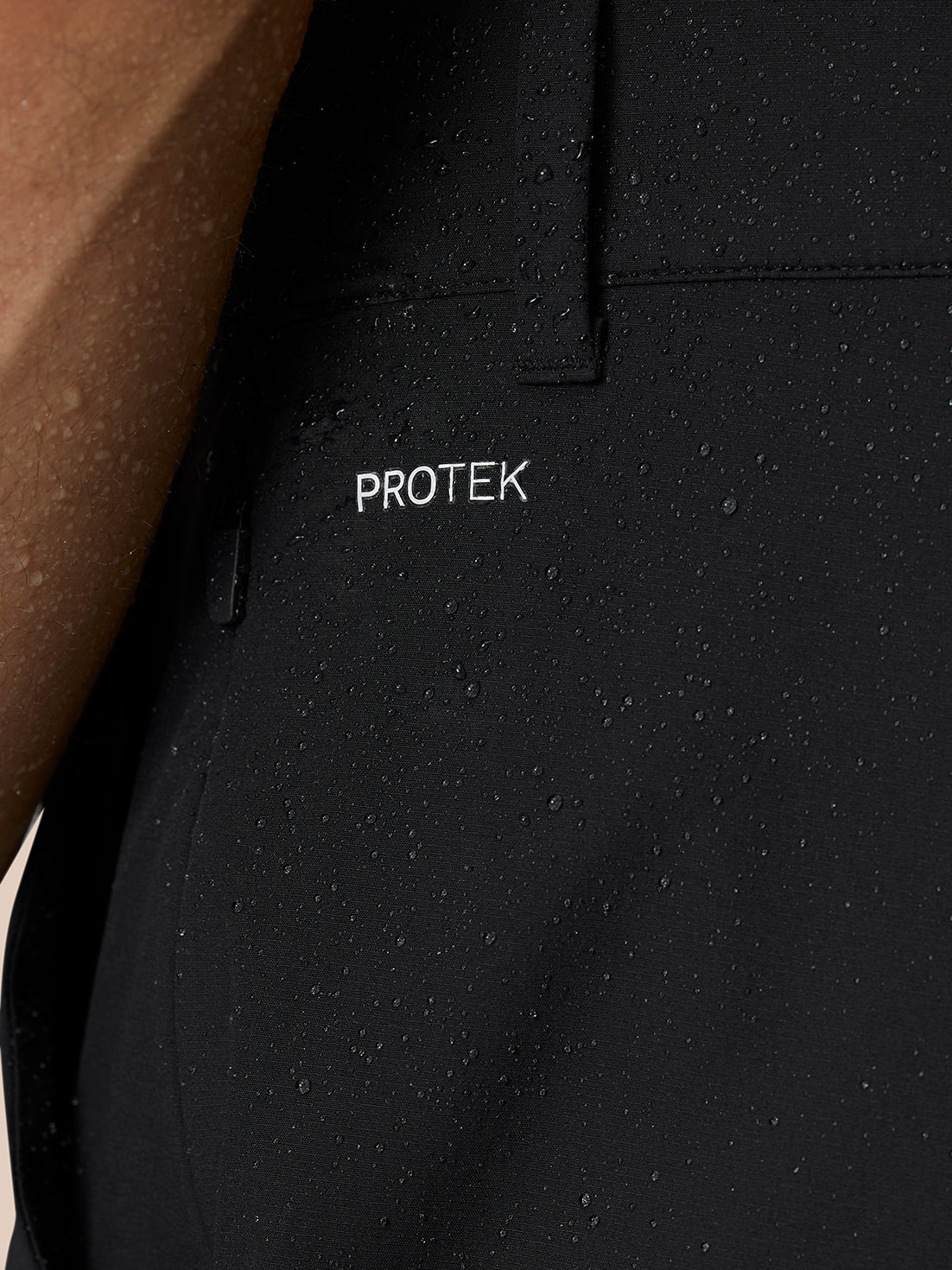 Close-up of black Golf Pinnacle Trousers fabric showing PROTEK water-resistant technology and a zip pocket.