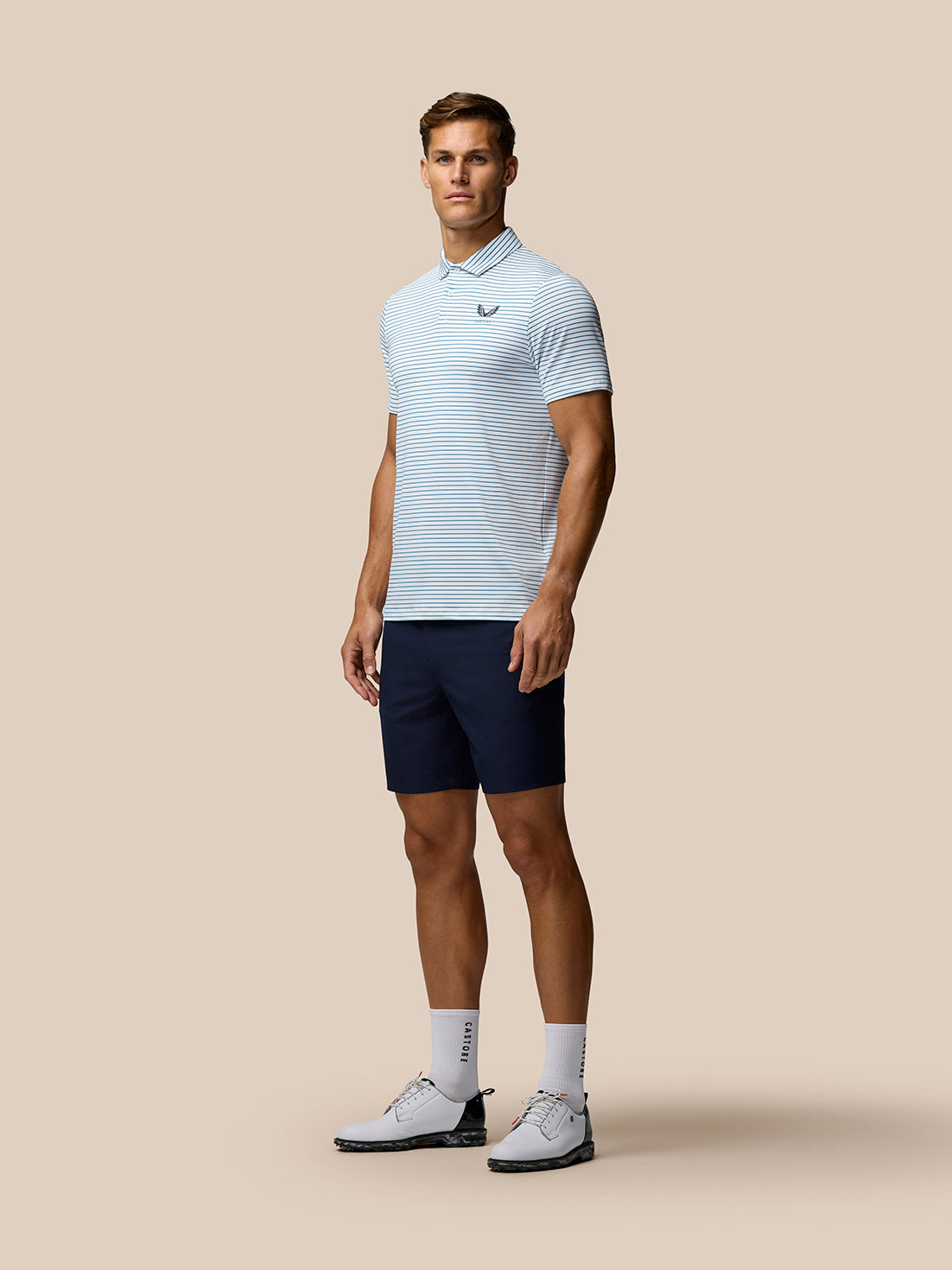 Male model wearing Club Golf Stripe Polo in white with light blue stripes and navy shorts