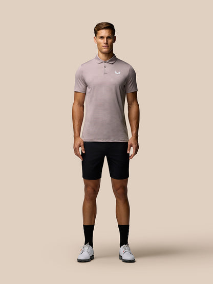 Full-body front view of a male model wearing pink yarn-dye stripe polo with white Castore logo, black shorts and white sneakers.