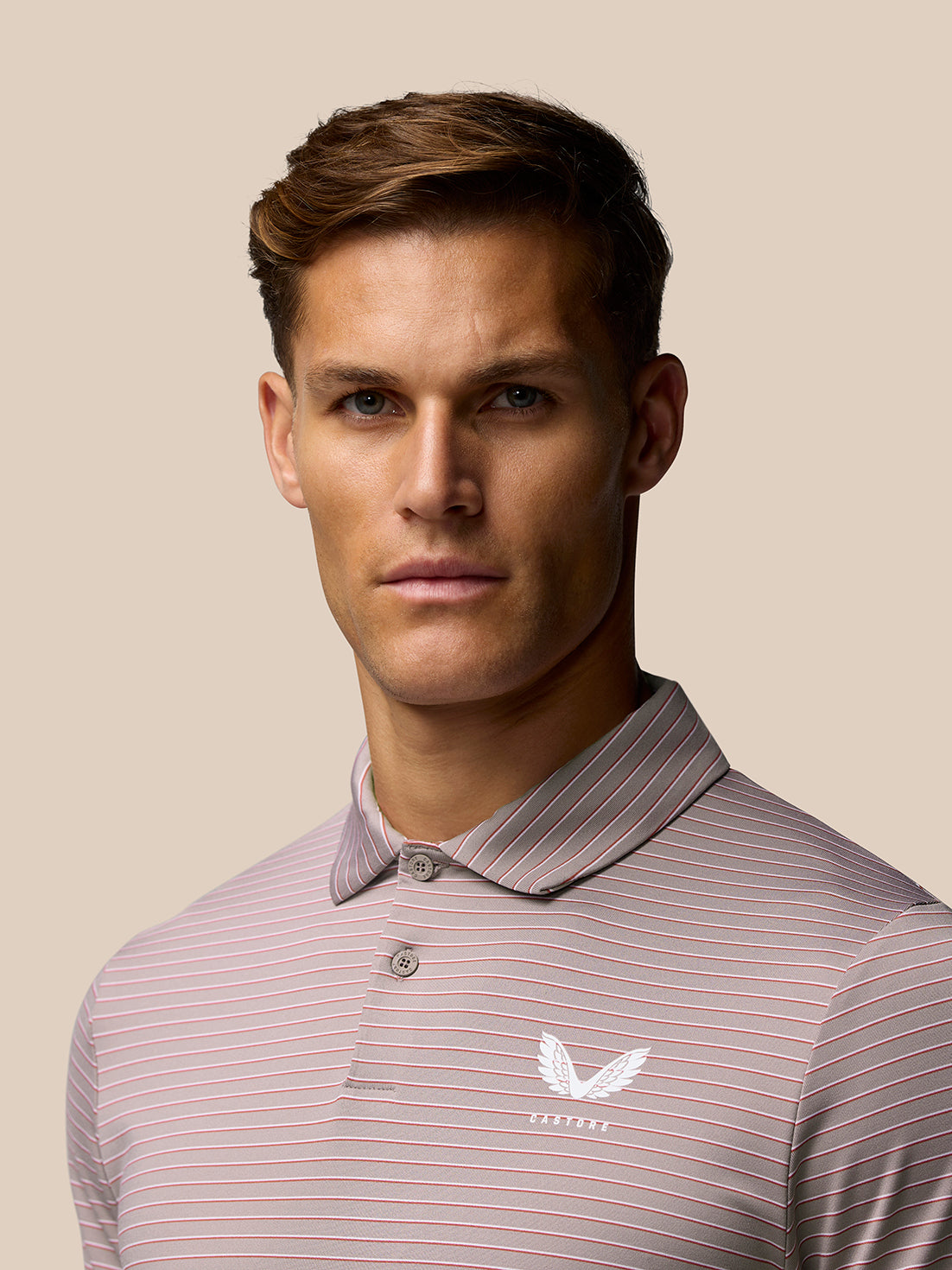 Male model wearing pink yarn-dye stripe golf polo with Castore logo on left chest, close up portrait.
