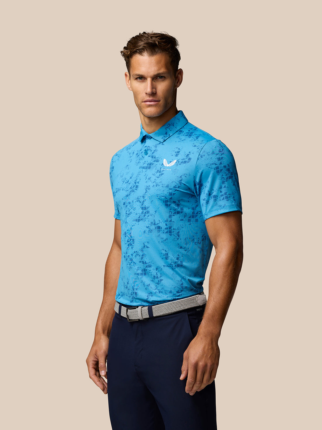Male model wearing blue geo print golf polo with Castore branding on the left chest