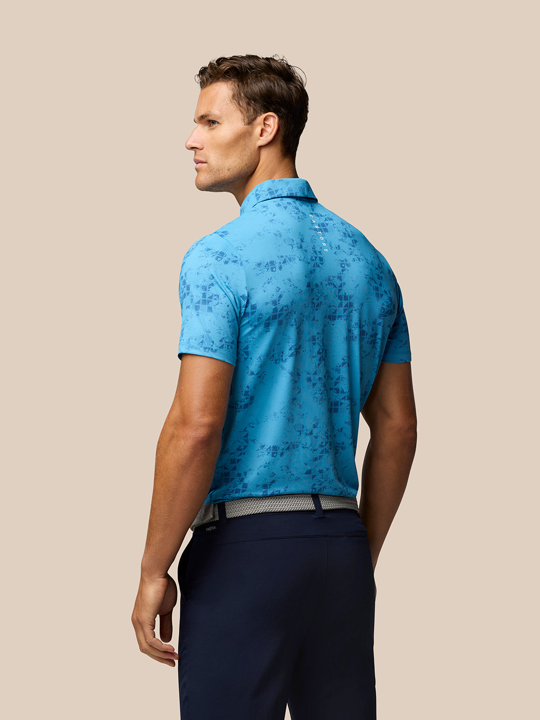 Back view of a golfer in a blue Geo Print Club Polo showing branding along the upper back.