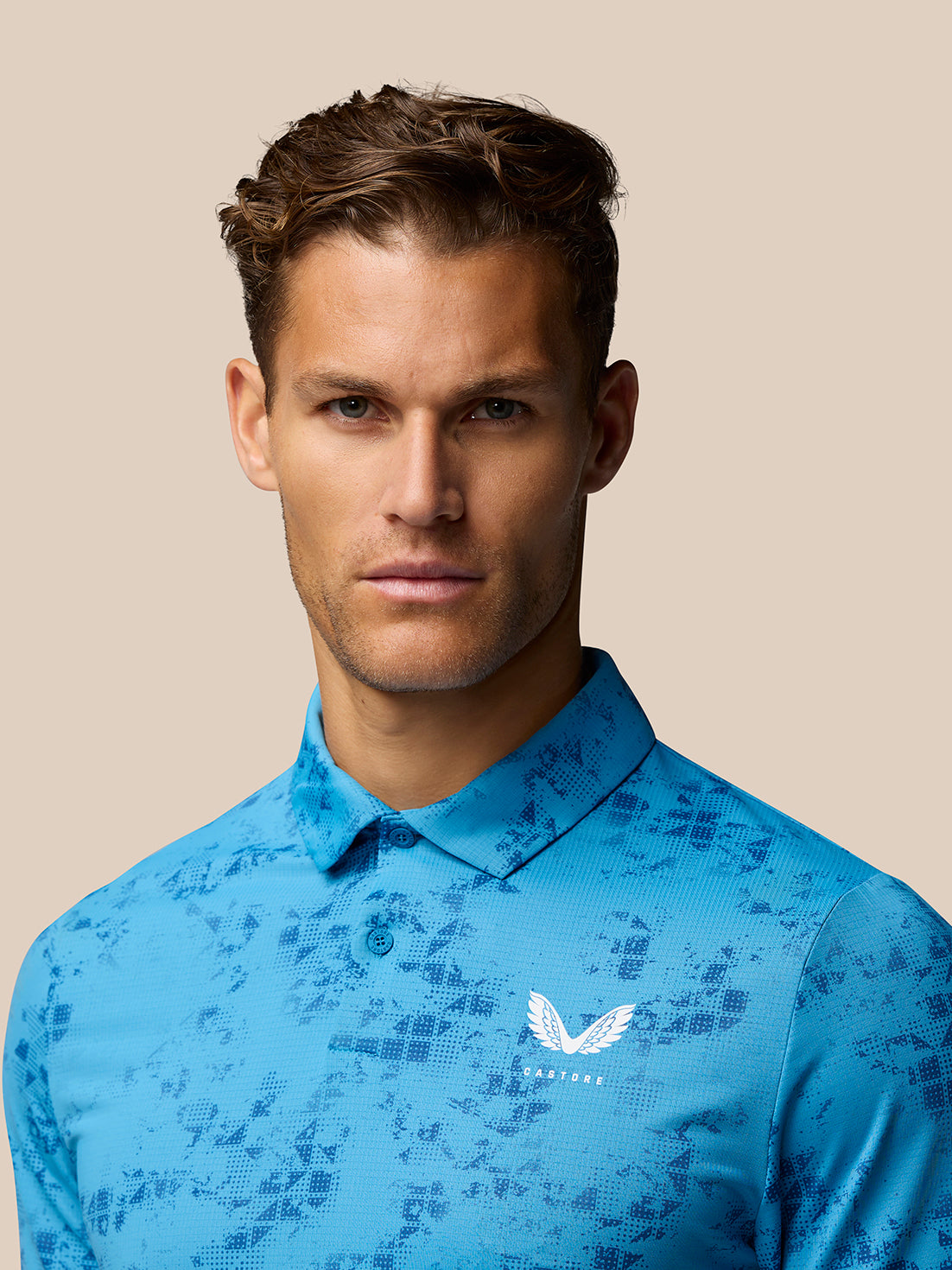 Close up of a male model wearing the blue Geo Print Club Polo with Castore logo on the left chest.