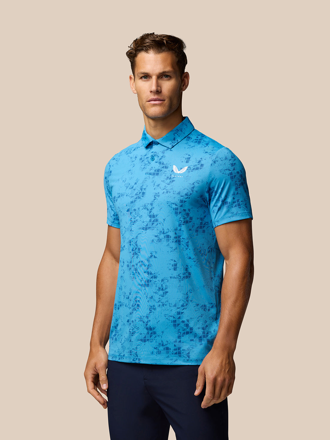 Athletic model wearing blue geo print polo with white logo on chest and navy pants