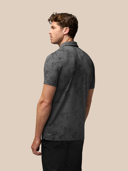Back view of a male model wearing charcoal geo print golf polo with Castore branding on upper back
