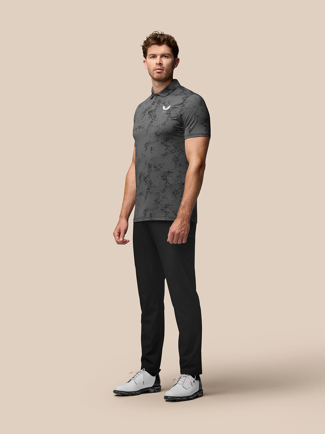 Male model wearing Club Golf Polo in charcoal with all over geo print and black pants