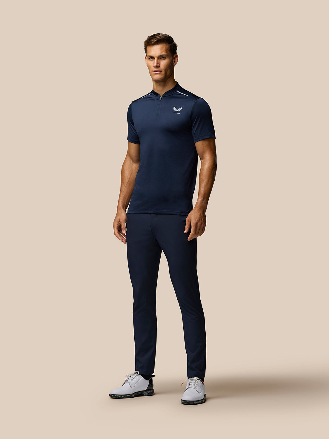 Full-length shot of a male model in midnight navy Pinnacle Varsity Polo with zip collar, navy trousers and white golf shoes.