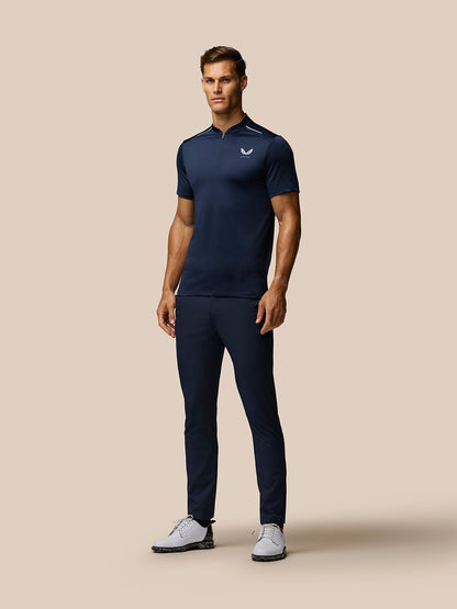 Full-length shot of a male model in midnight navy Pinnacle Varsity Polo with zip collar, navy trousers and white golf shoes.