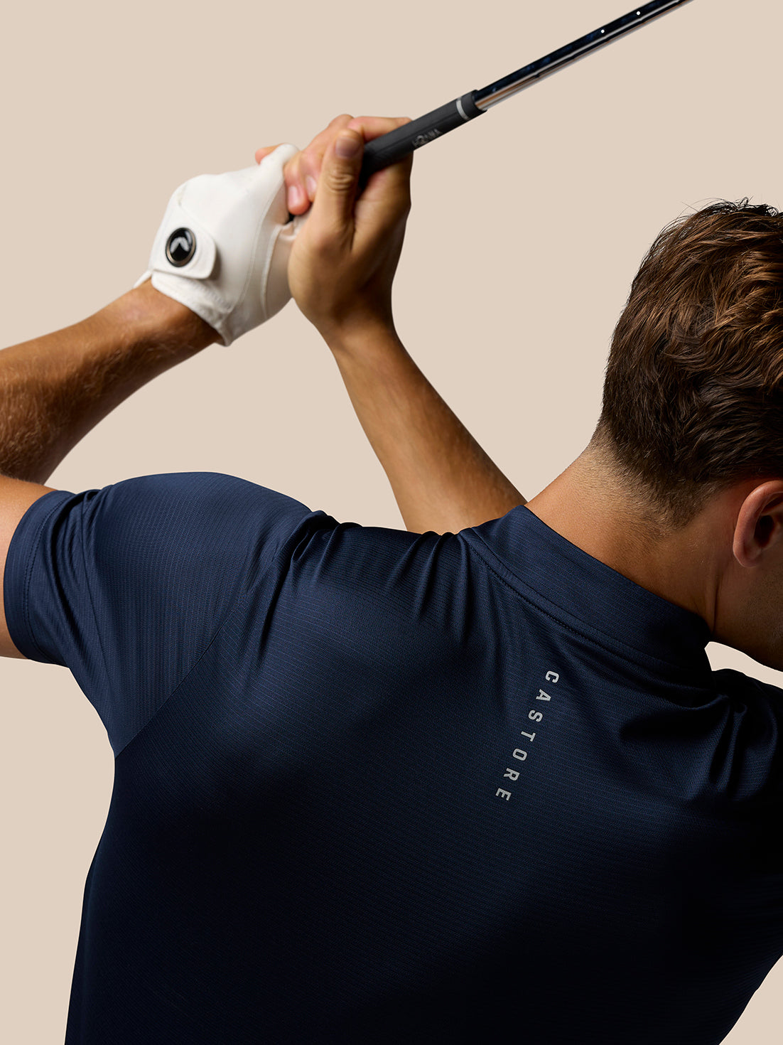 Male golfer in midnight navy Pinnacle Varsity Polo grips a golf club overhead, wearing a white left-hand glove.