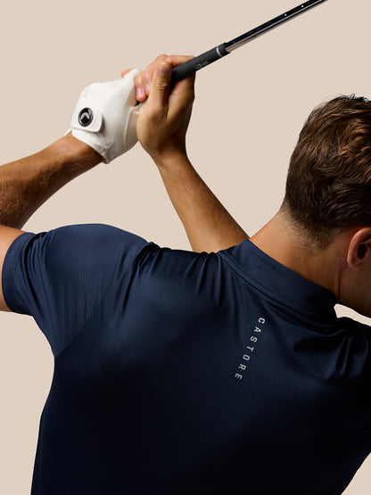 Male golfer in midnight navy Pinnacle Varsity Polo grips a golf club overhead, wearing a white left-hand glove.