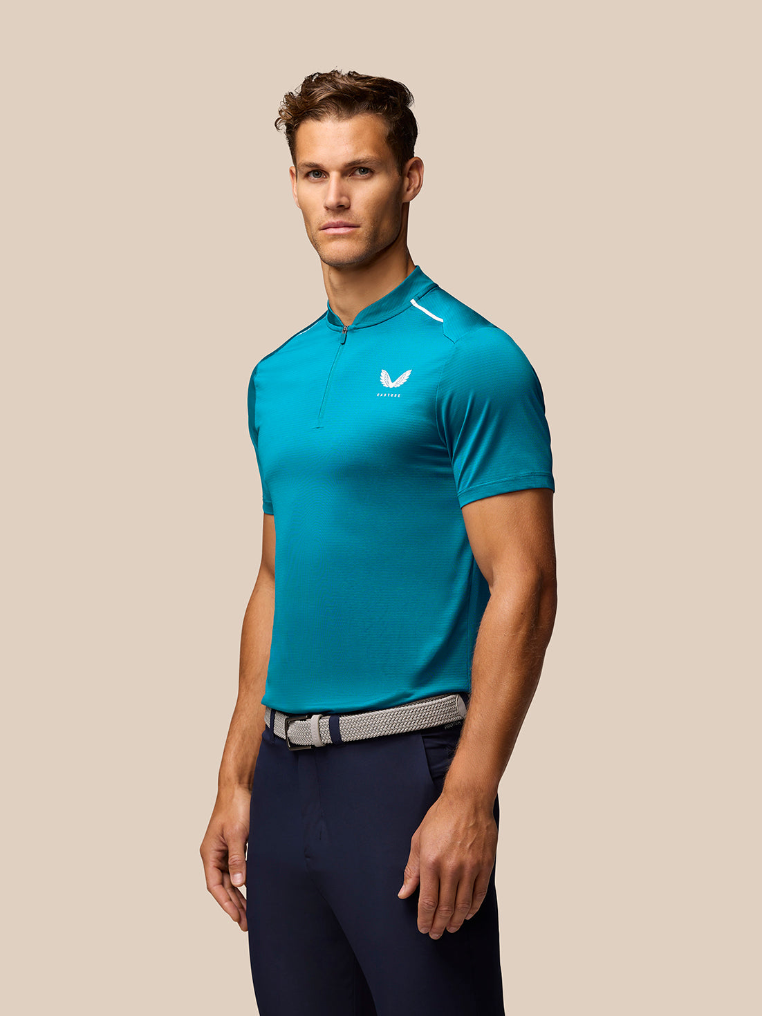 Male model in teal Pinnacle Varsity Polo with quarter zip, paired with navy pants