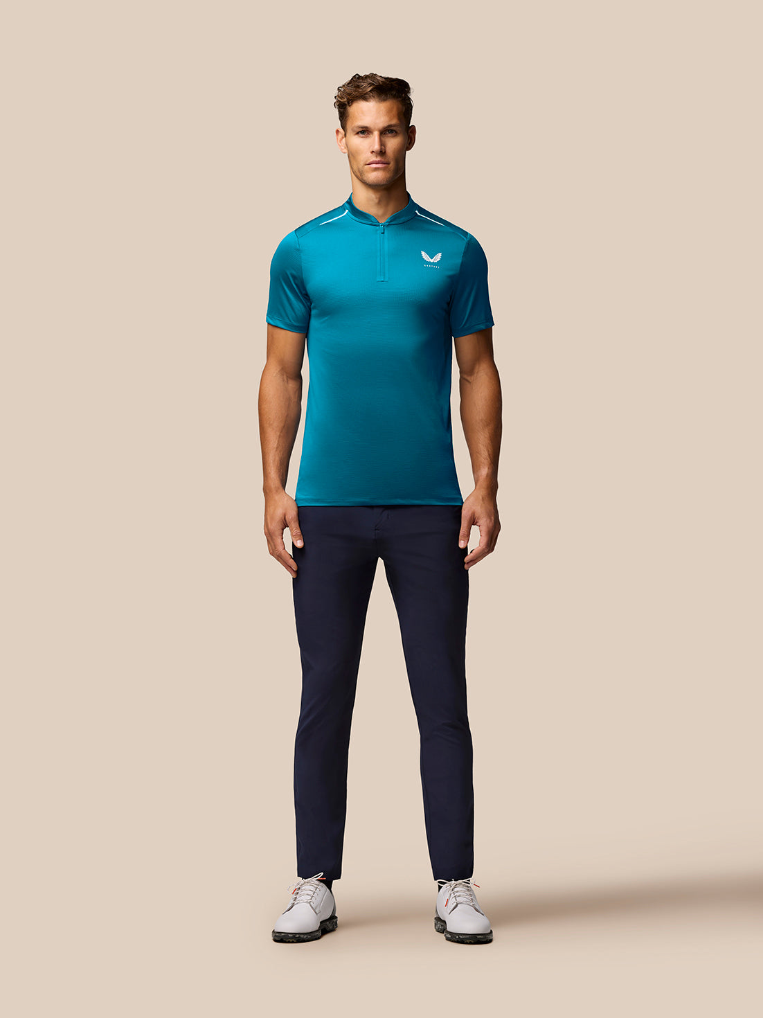 Full-body front view of a man wearing a teal Pinnacle Golf Varsity Polo with zip placket and Castore branding on the chest