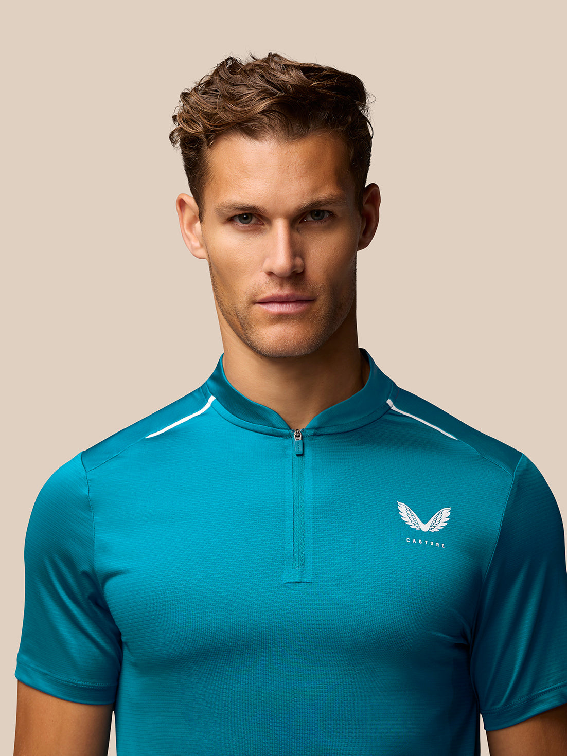 Male model wearing teal Pinnacle Golf Varsity Polo with front zip and Castore logo on the chest