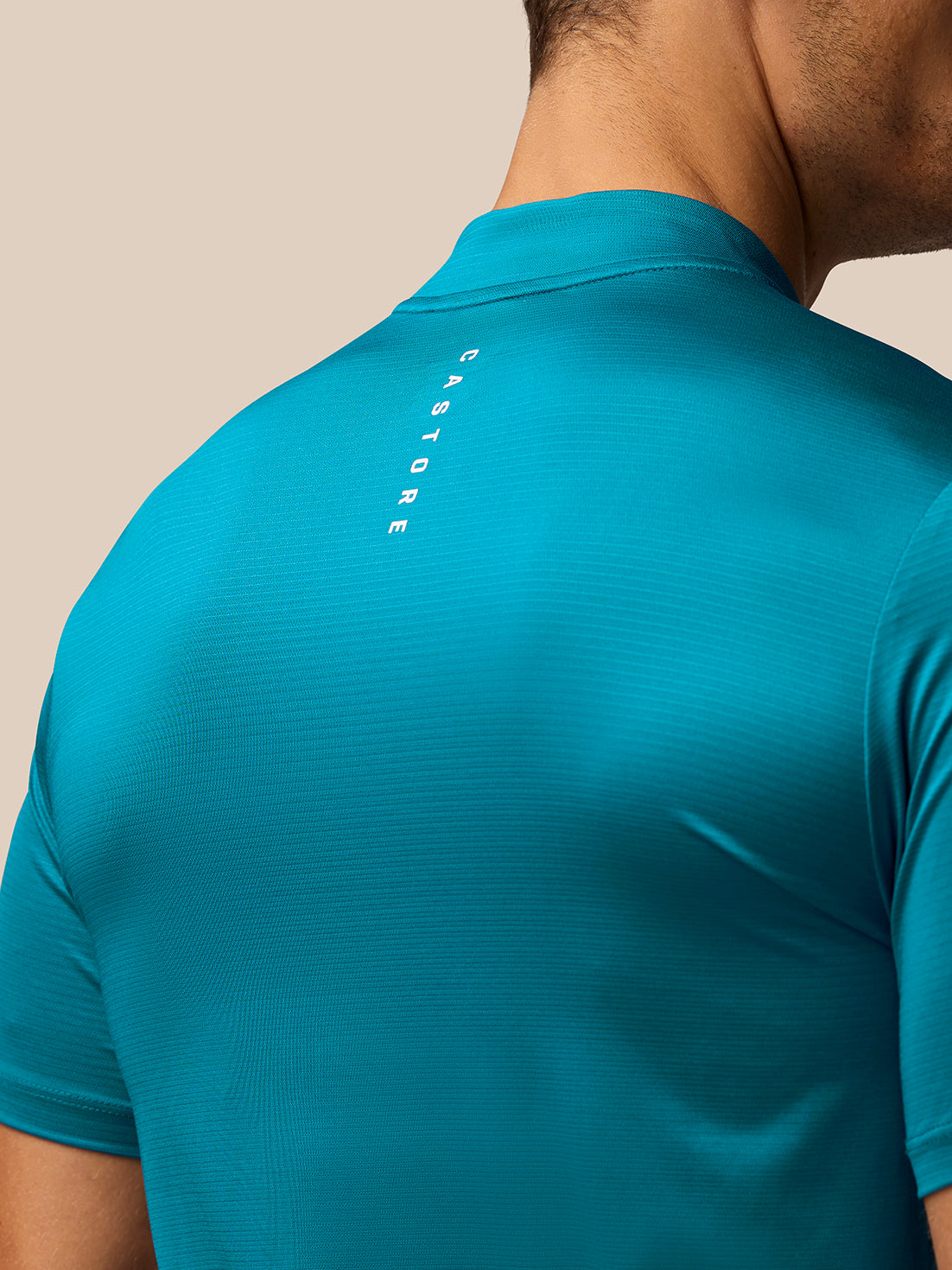 Close-up of the back of a teal Pinnacle Golf Varsity Polo showing vertical Castore branding along the upper back