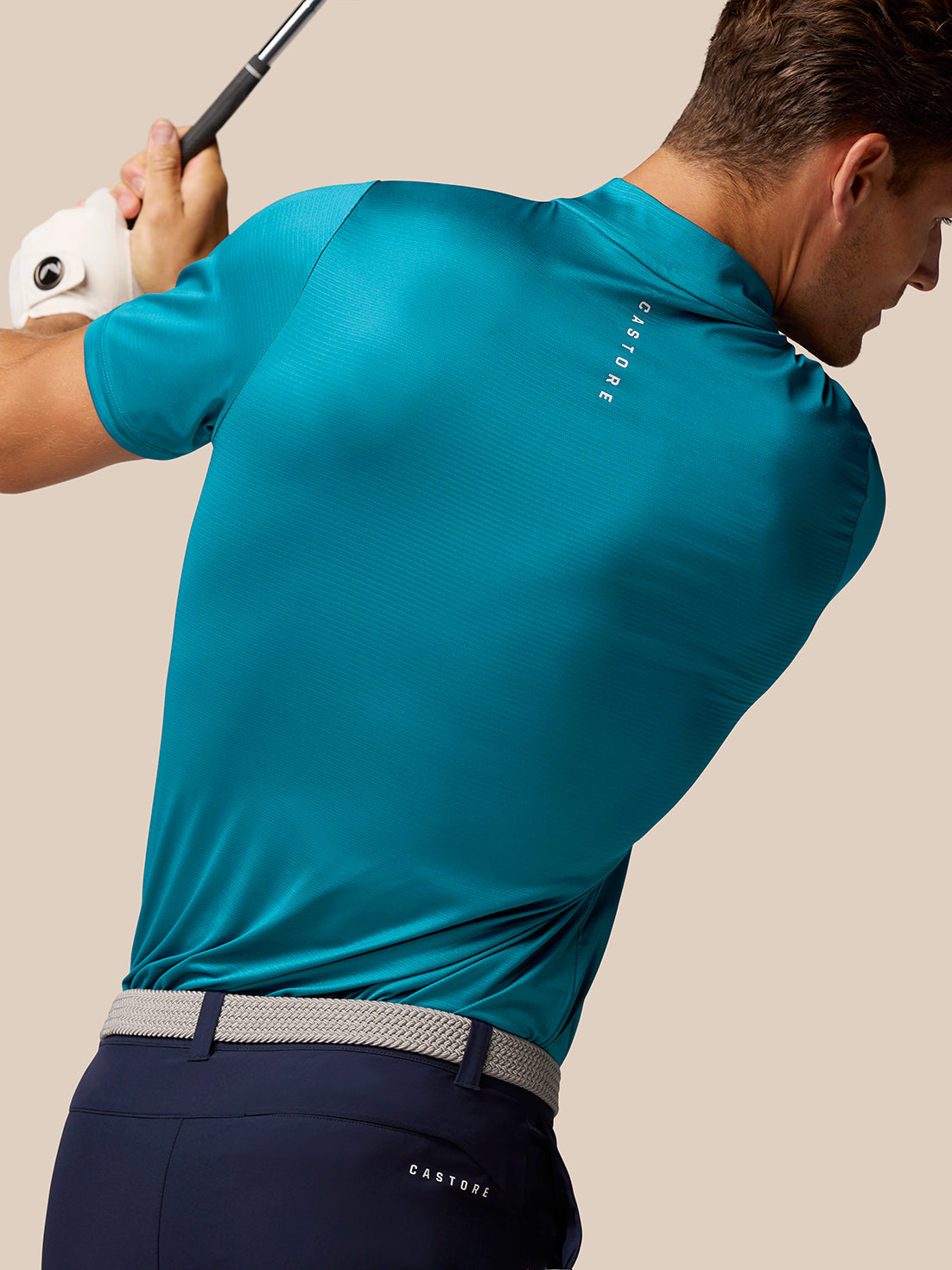 Side view of male golfer in teal Pinnacle Varsity Polo mid swing with Castore branding on upper back