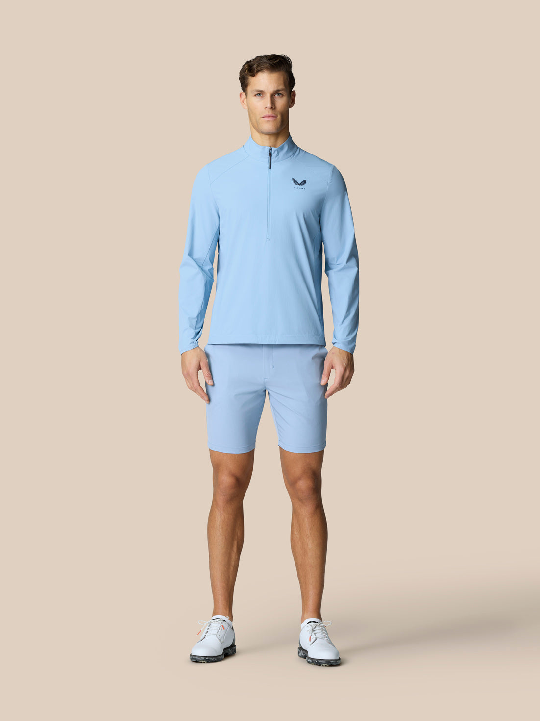 Full-body view of a man wearing a sky blue Golf Flex Jacket with matching shorts on a beige background