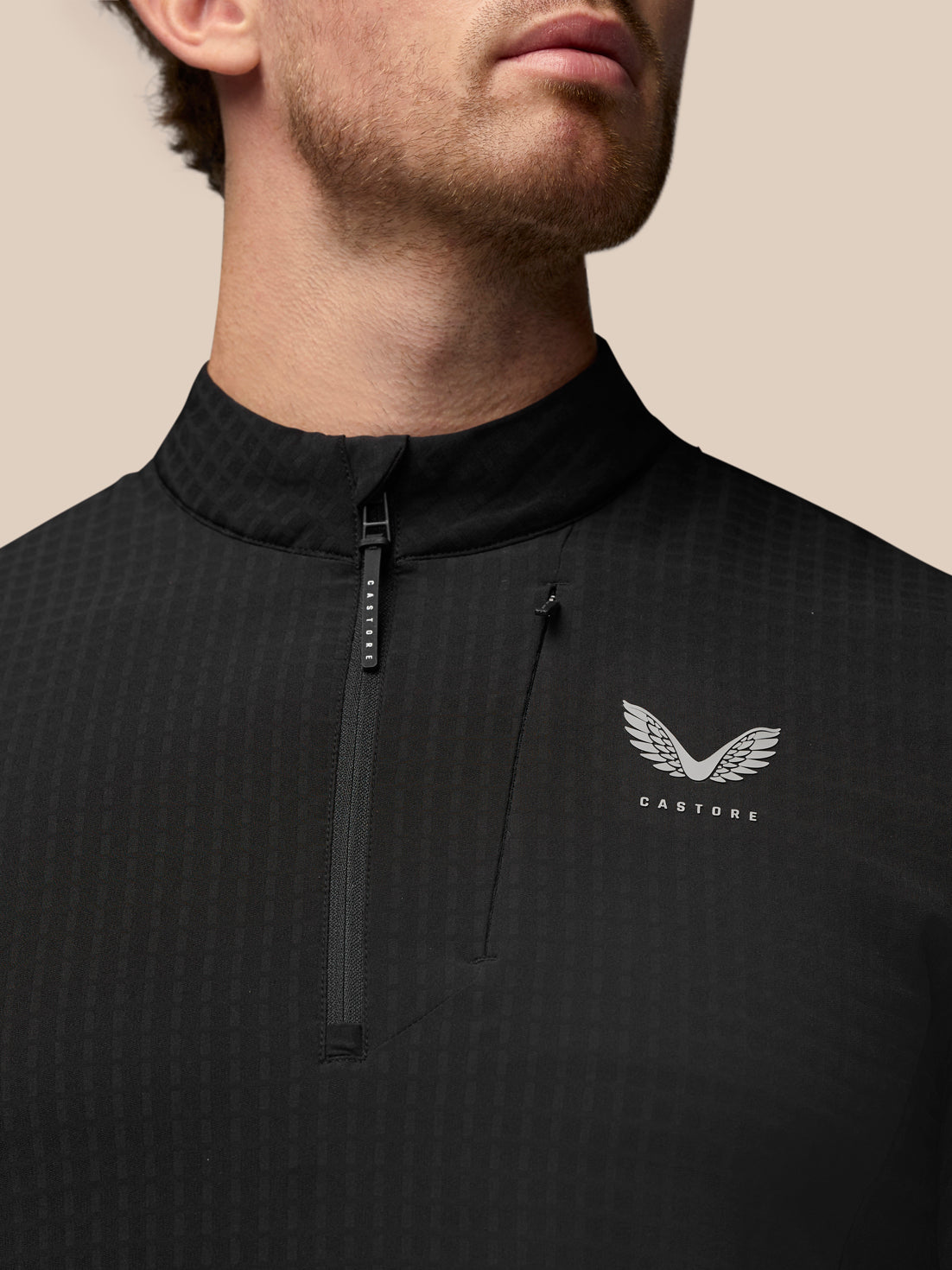 Close up of black golf top with stand collar and half zip, showing Castore logo on the chest and Protek branding on the cuff