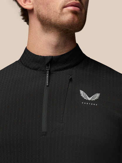 Close up of black golf top with stand collar and half zip, showing Castore logo on the chest and Protek branding on the cuff
