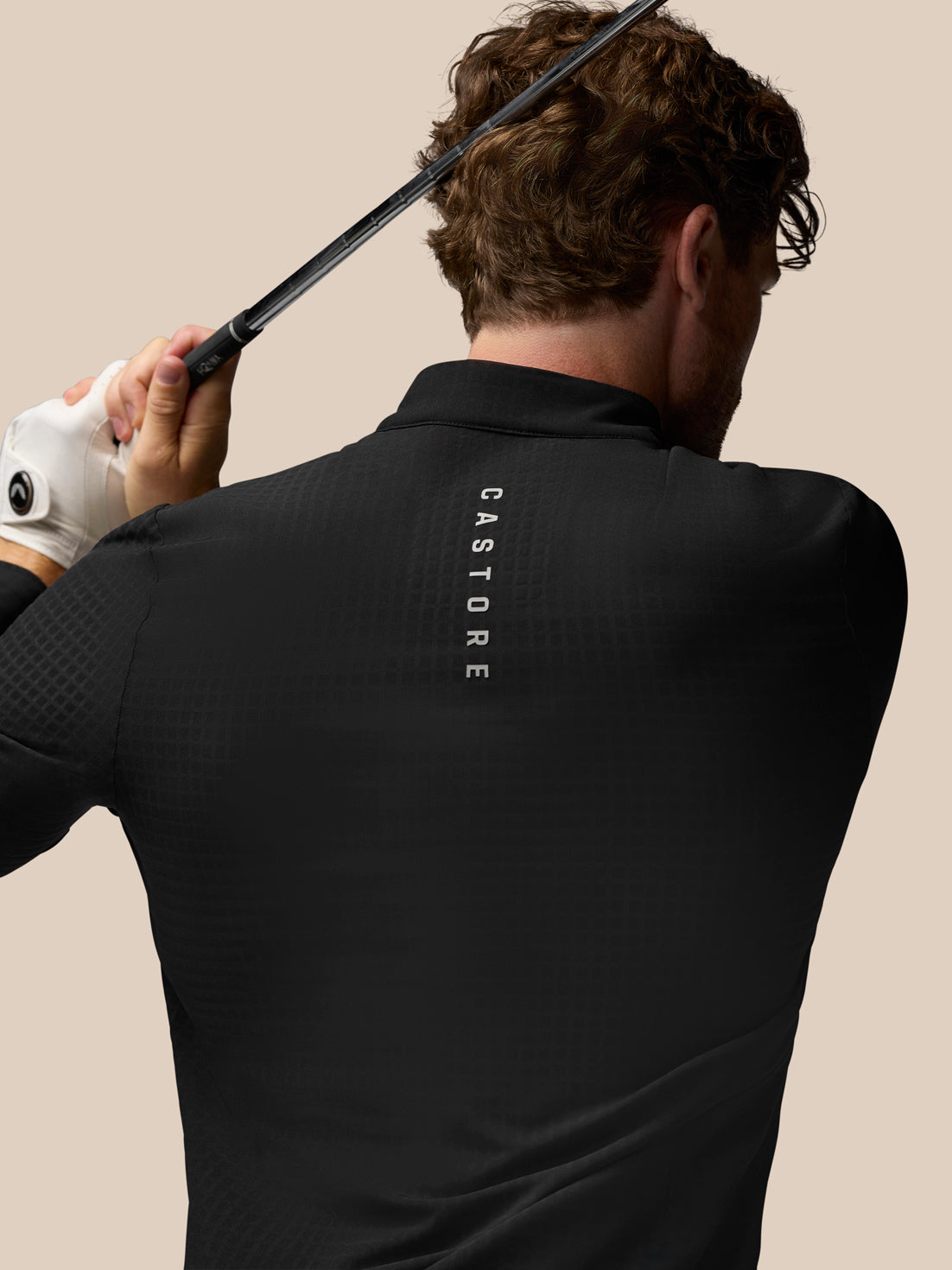 Back view of black golf top on a model with vertical Castore branding along the upper back