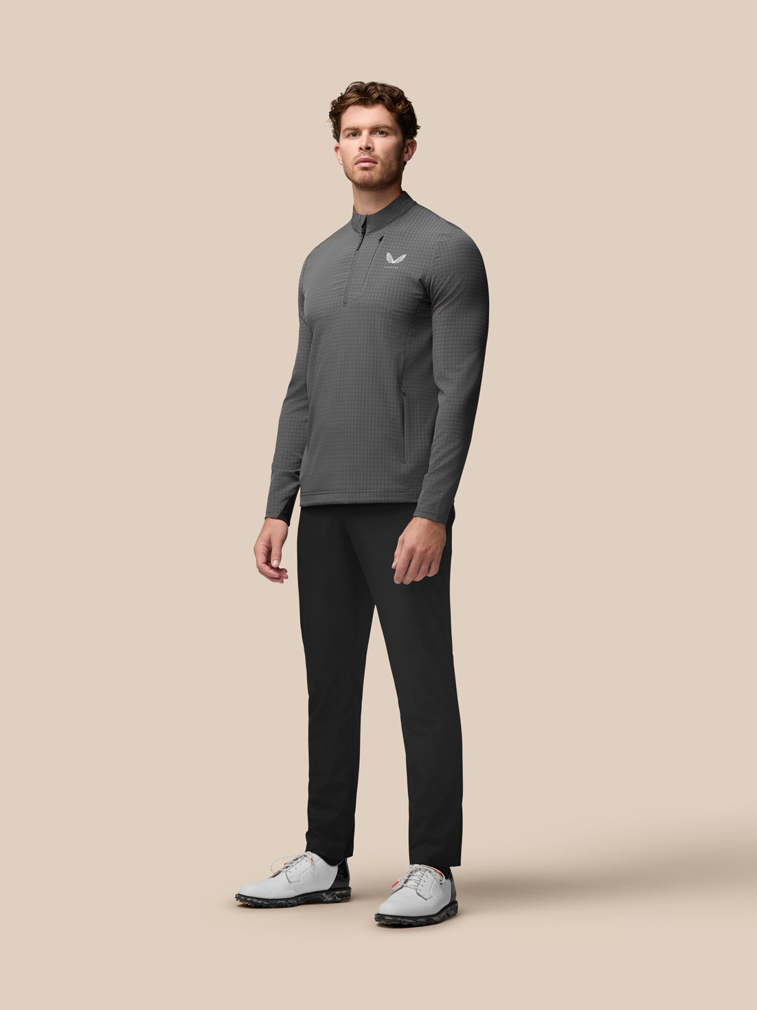 Grey golf 1/2 zip top on a model with stand collar and zip side pockets; Castore branding on chest.