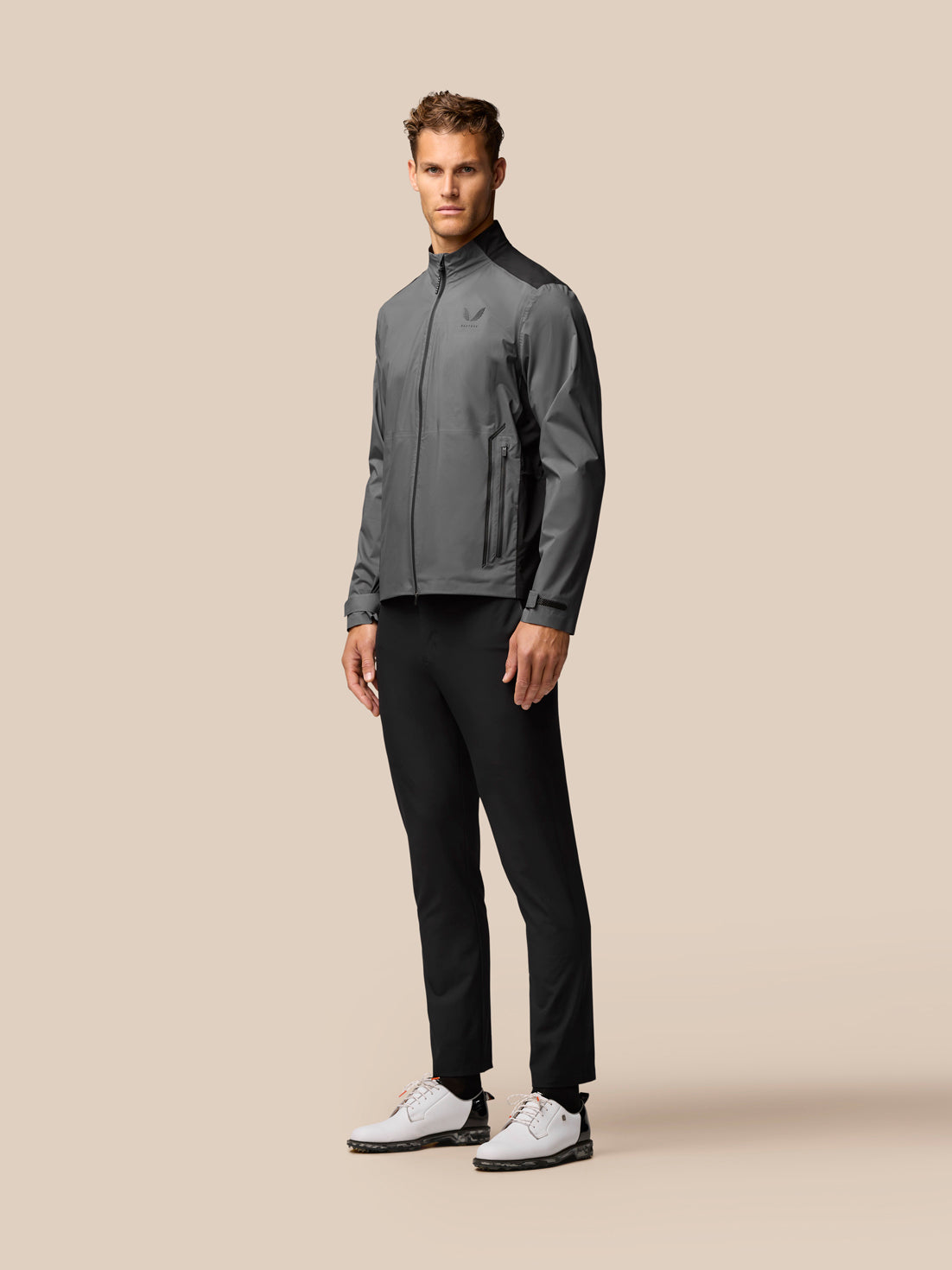 Male model wearing Gunmetal Golf Waterproof Jacket with black shoulder panels, front zip and zipped pockets, standing in a neutral studio.