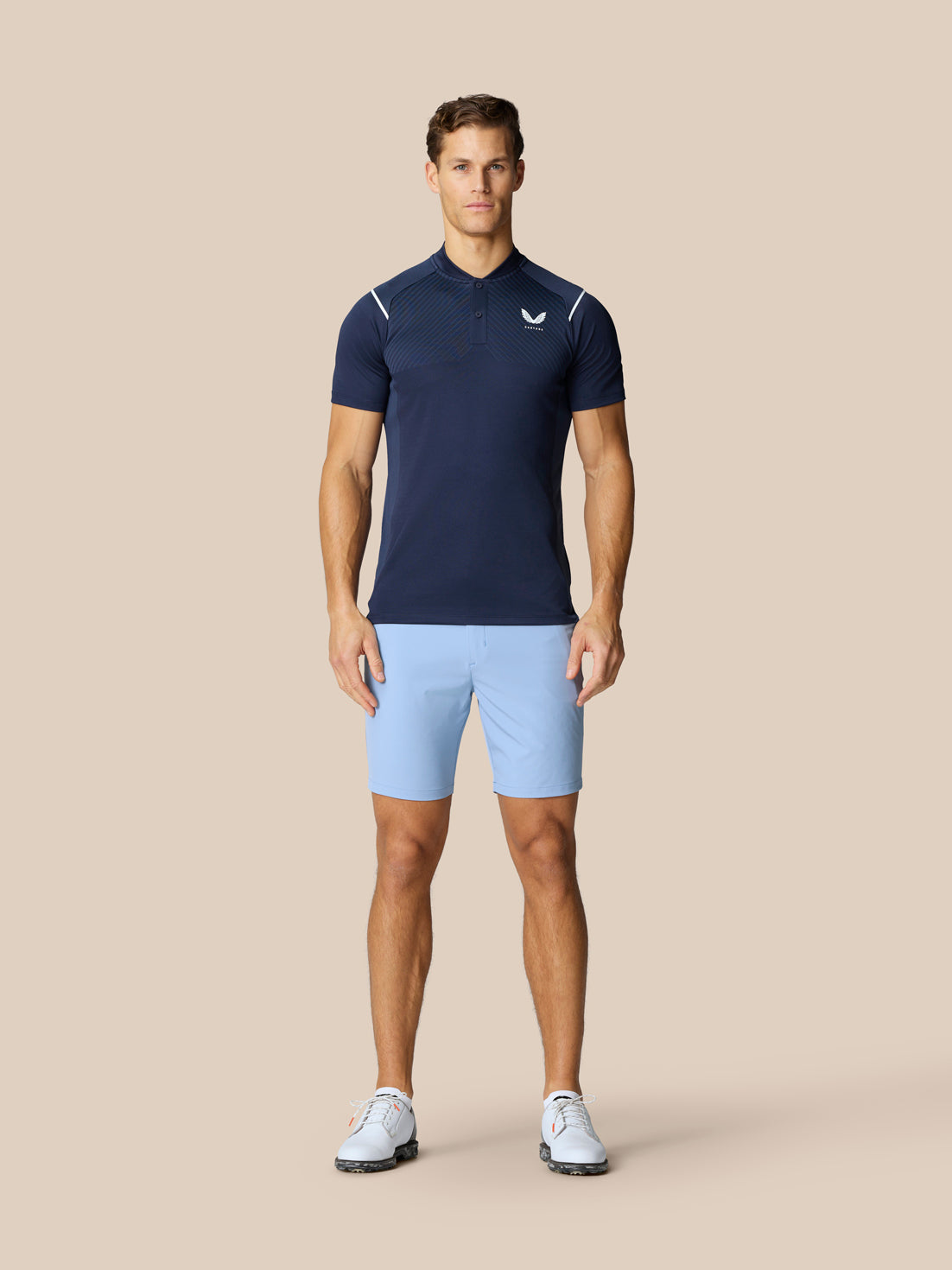 Male model wearing Pinnacle Golf LVS Polo in navy with vented chest panels paired with light blue shorts.
